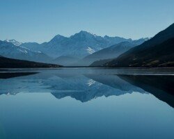 Mountain lake reflecting snow-capped peaks under blue sky