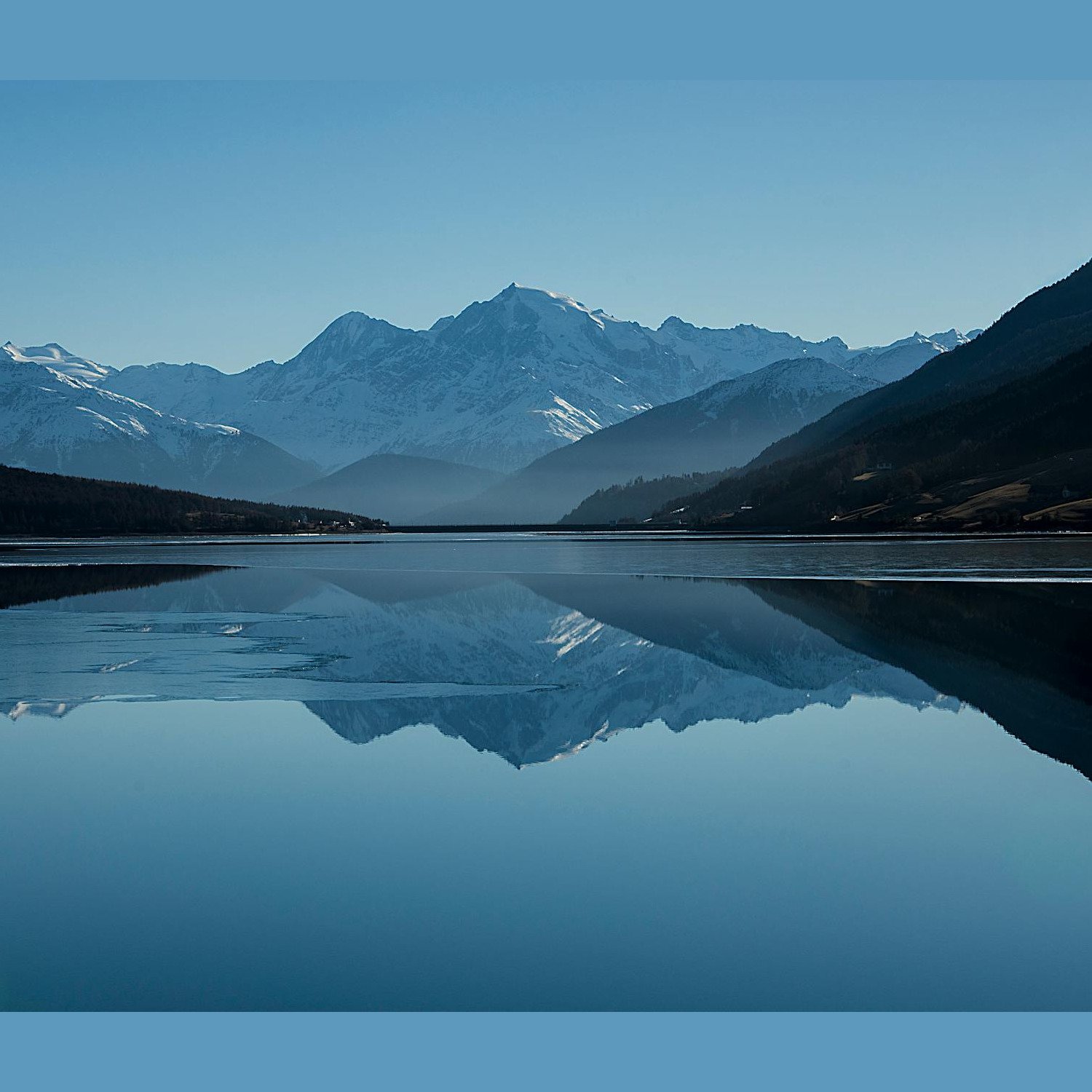 Mountain lake reflecting snow-capped peaks under blue sky
